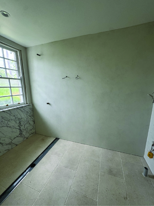 - Luxury Linings Seamless grey MicroCement wall finish in a modern bathroom renovation, creating a smooth, waterproof surface next to a window and tiled floor.